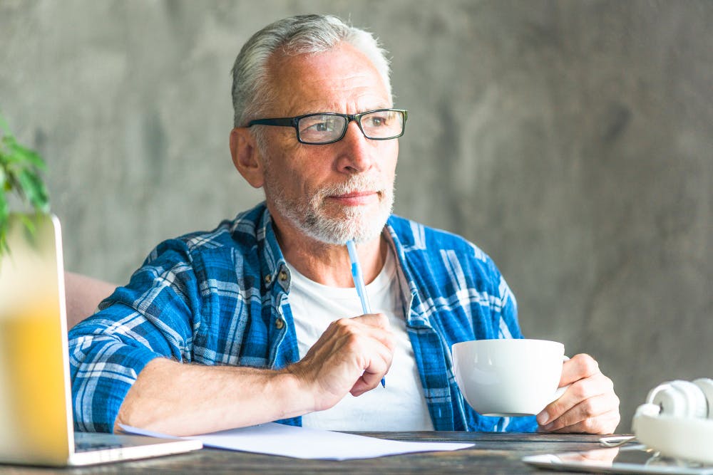 thoughtful senior man holding pen and coffee