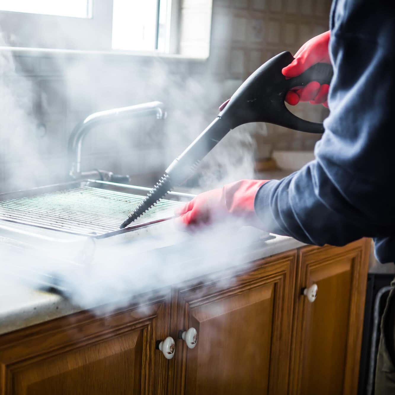 Gloved cleaner washing oven with steamer at home closeup